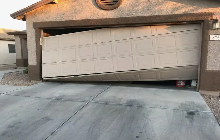 Damaged garage door hanging unevenly with a bent lower section
