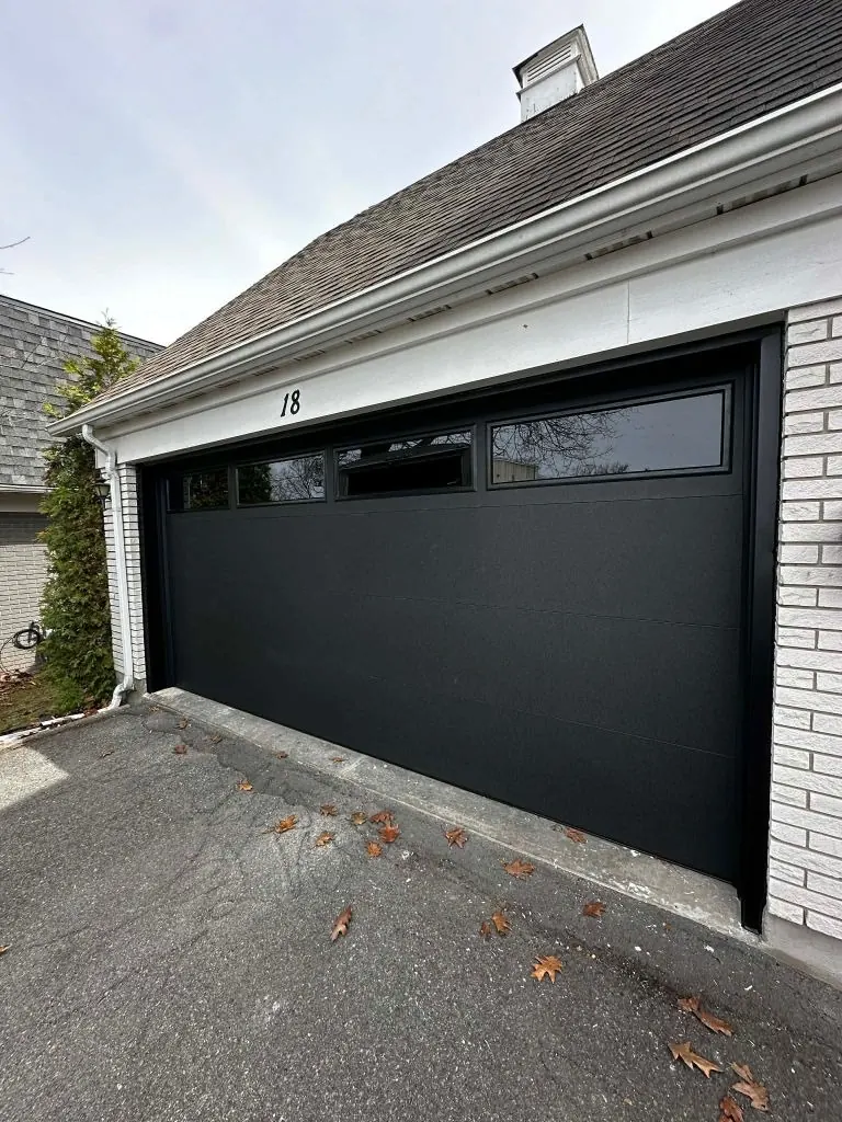 Black garage door with upper windows on a light-coloured home